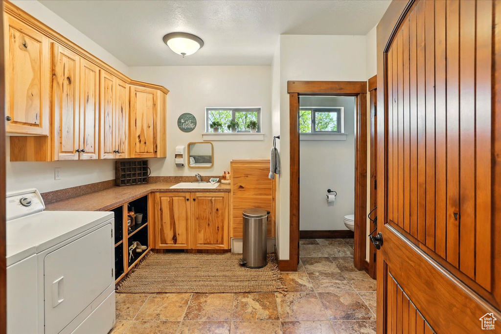 Washroom featuring a sink, washer and dryer, and light stone finish floors
