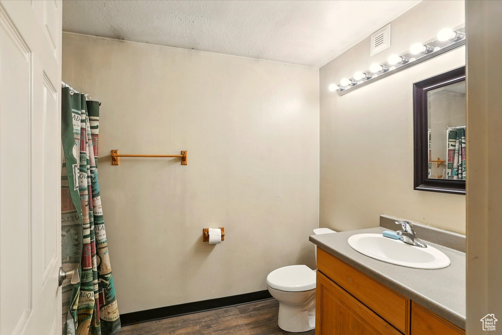 Full bathroom with toilet, wood finished floors, vanity, and a textured ceiling