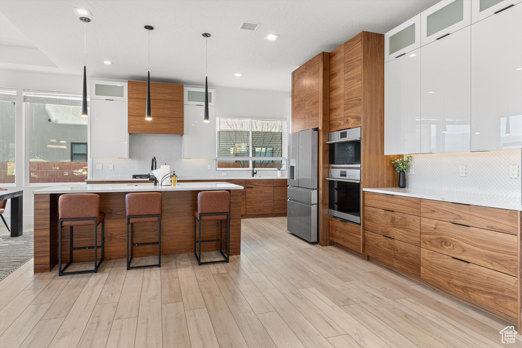 Kitchen featuring modern cabinets, brown cabinetry, appliances with stainless steel finishes, a breakfast bar area, and light countertops