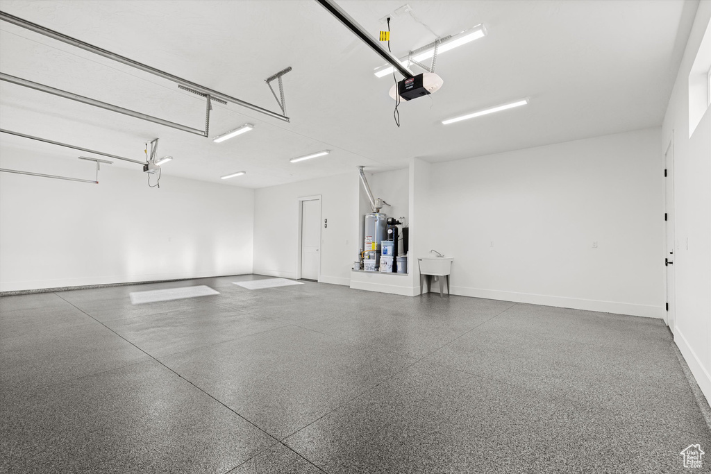 Garage with a garage door opener, baseboards, and gas water heater