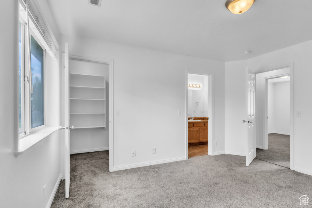 Unfurnished bedroom with carpet flooring, baseboards, a walk in closet, ensuite bathroom, and a closet