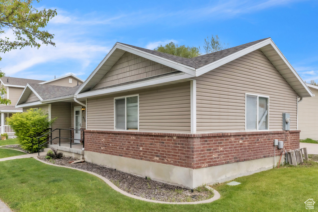 View of property exterior with brick siding, a yard, and roof with shingles