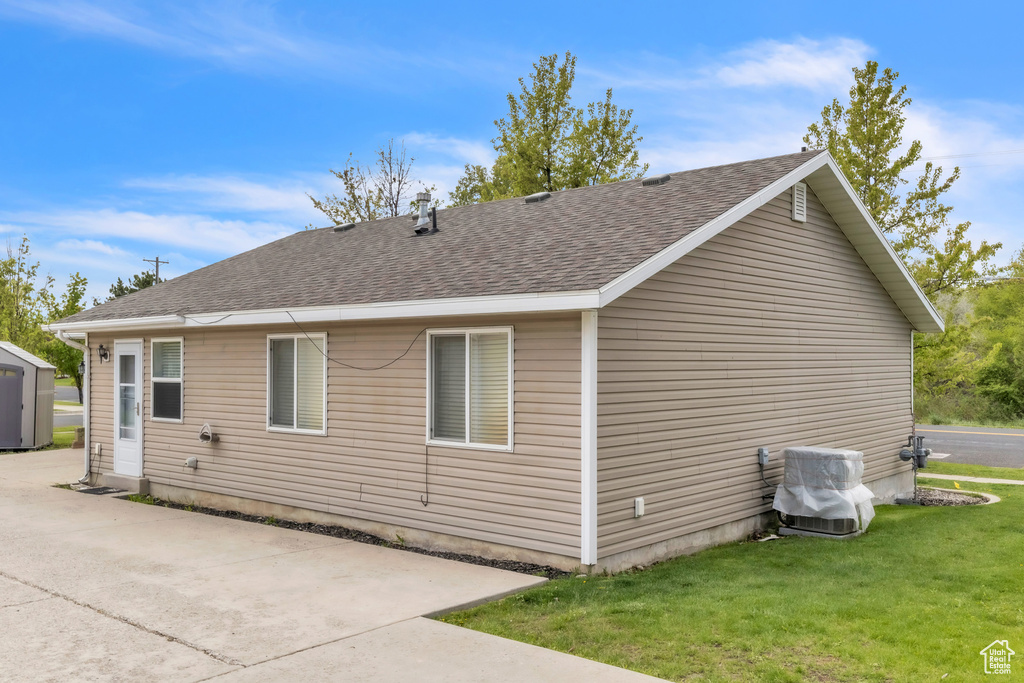 Back of property featuring a shingled roof, a lawn, and a patio area
