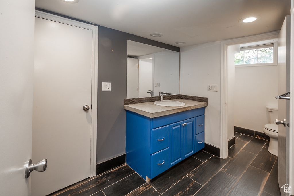 Bathroom featuring toilet, vanity, recessed lighting, baseboards, and wood finished floors