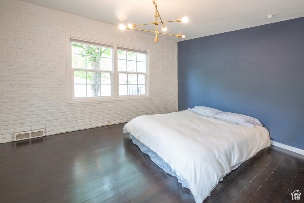 Bedroom featuring a chandelier, brick wall, and dark wood finished floors