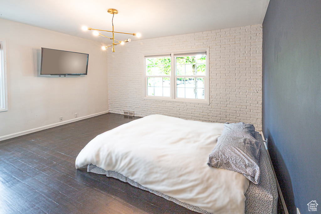 Bedroom featuring a chandelier, wood finished floors, brick wall, and baseboards