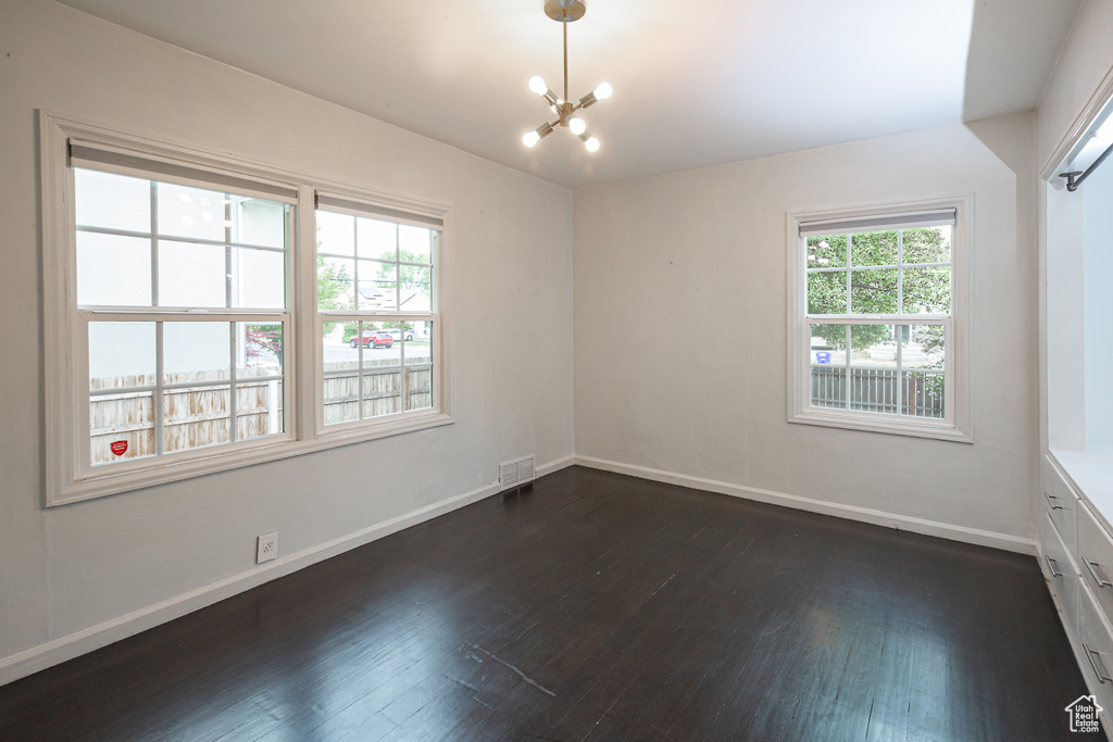 Spare room featuring dark wood finished floors, a chandelier, and baseboards
