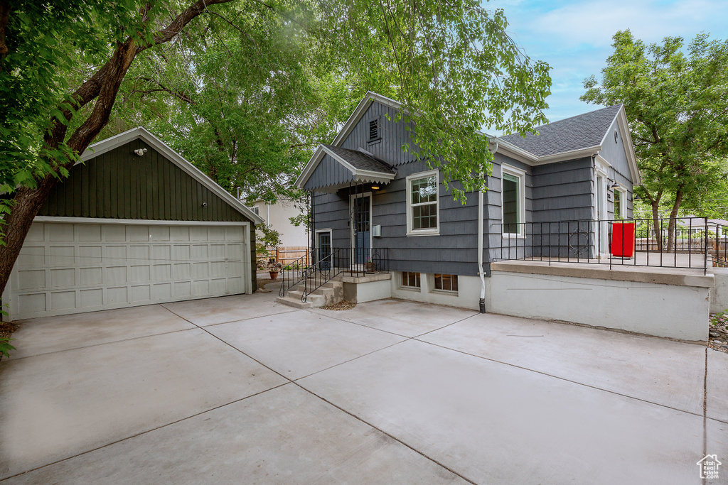 View of front facade with roof with shingles, a garage, an outbuilding, and fence