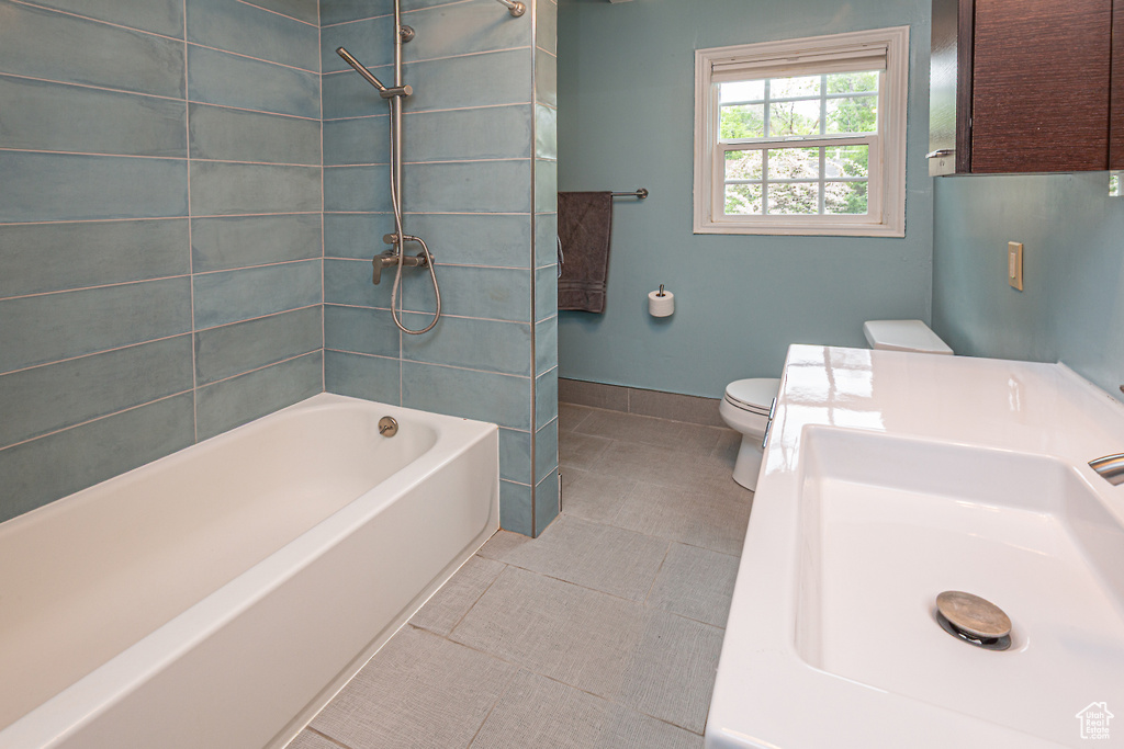 Bathroom featuring a sink, toilet, tile patterned flooring, baseboards, and shower / bathtub combination