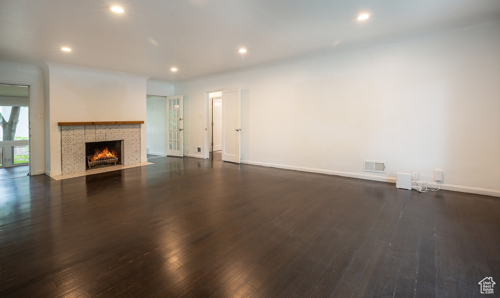 Unfurnished living room with dark wood-style flooring, a tiled fireplace, recessed lighting, and baseboards