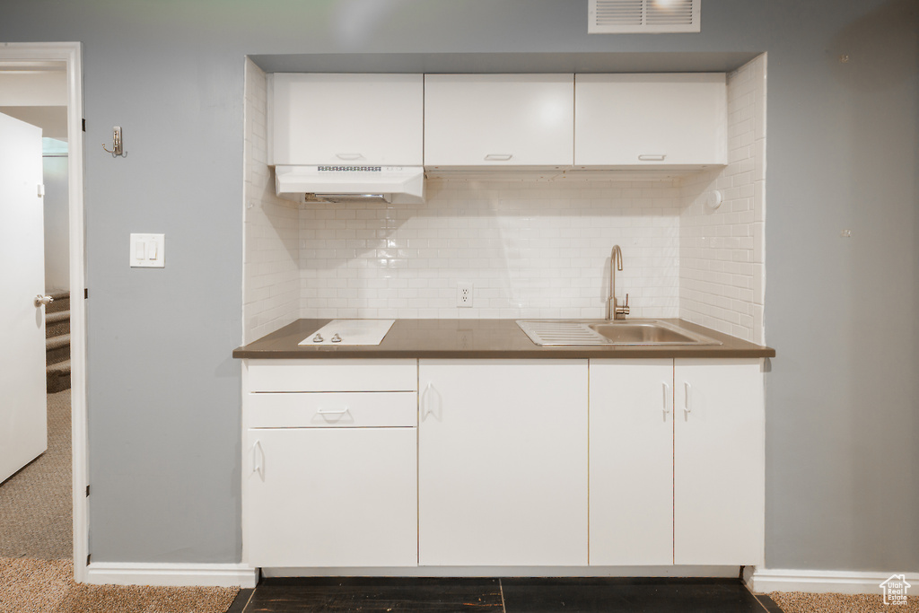 Kitchen with under cabinet range hood, a sink, tasteful backsplash, white cabinetry, and dark countertops