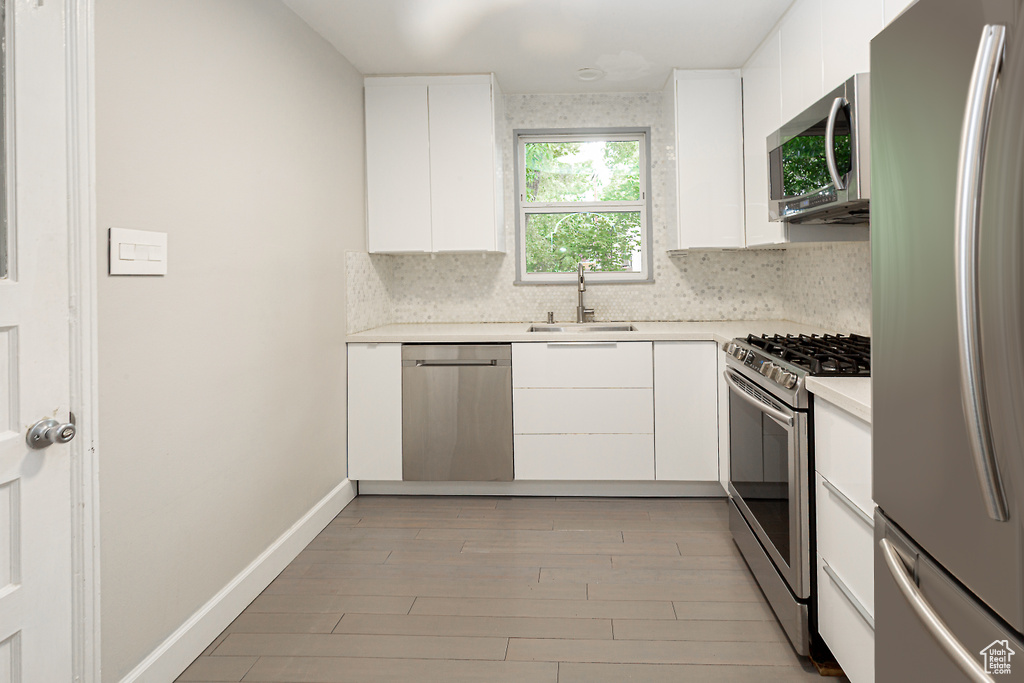 Kitchen with stainless steel appliances, a sink, light countertops, decorative backsplash, and white cabinetry