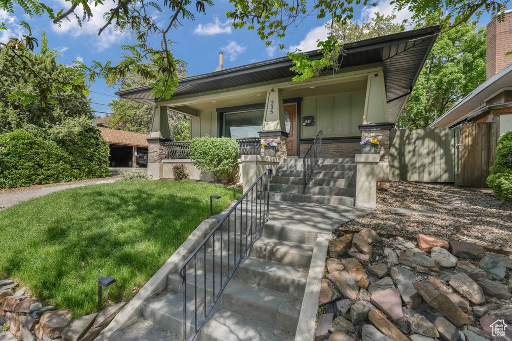 View of front of home featuring covered porch, a front lawn, stone siding, and board and batten siding
