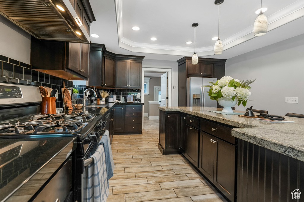 Kitchen with appliances with stainless steel finishes, wall chimney range hood, ornamental molding, decorative backsplash, and wood tiled floors