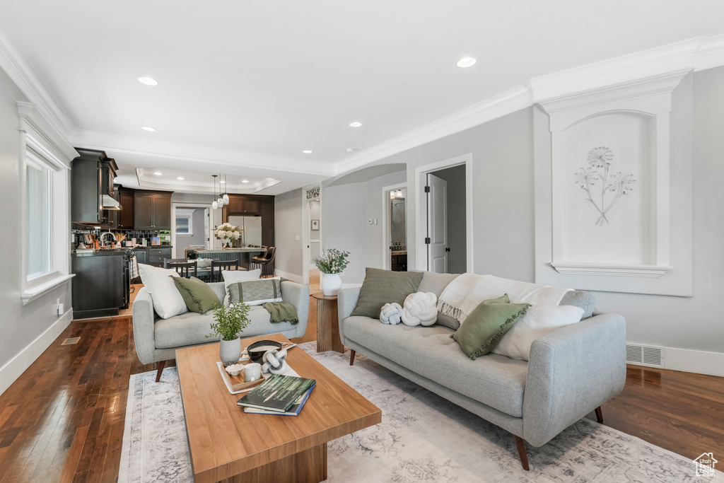 Living area featuring dark wood-style floors, recessed lighting, crown molding, arched walkways, and baseboards