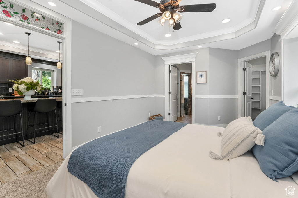 Bedroom with light wood-style flooring, ornamental molding, recessed lighting, a tray ceiling, and ceiling fan