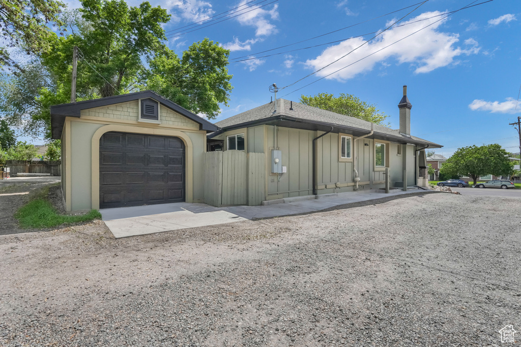 Single story home featuring board and batten siding, a garage, fence, driveway, and an outdoor structure