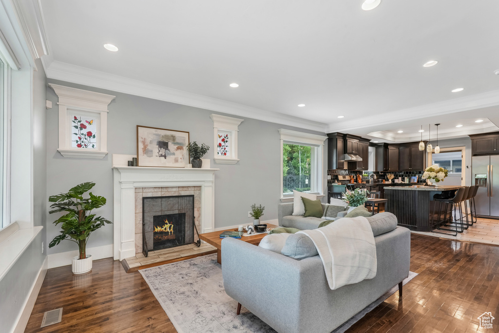 Living area with ornamental molding, dark wood-style flooring, a tiled fireplace, recessed lighting, and baseboards