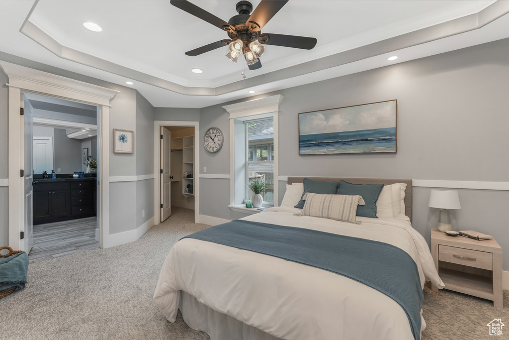 Bedroom with light colored carpet, a tray ceiling, recessed lighting, a spacious closet, and ensuite bath