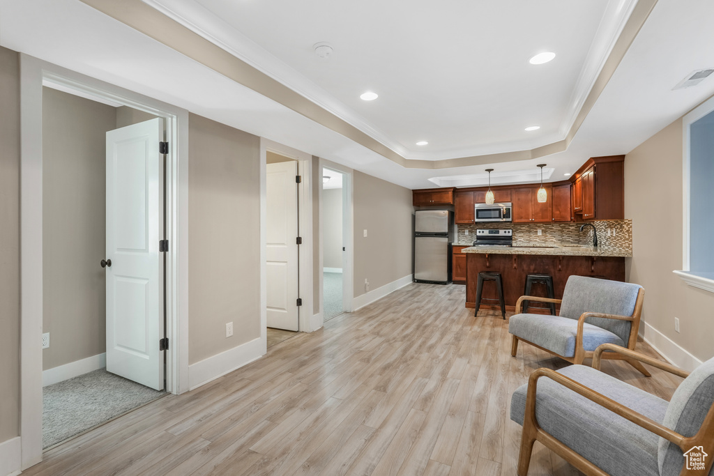 Living area featuring light wood-type flooring, baseboards, a raised ceiling, and recessed lighting