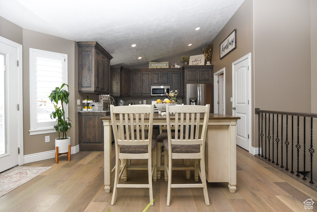 Kitchen featuring appliances with stainless steel finishes, dark brown cabinetry, light wood finished floors, vaulted ceiling, and a kitchen island