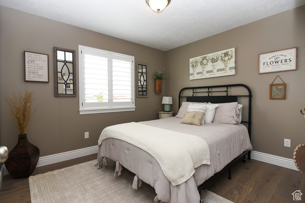 Bedroom with wood finished floors, baseboards, and a textured ceiling