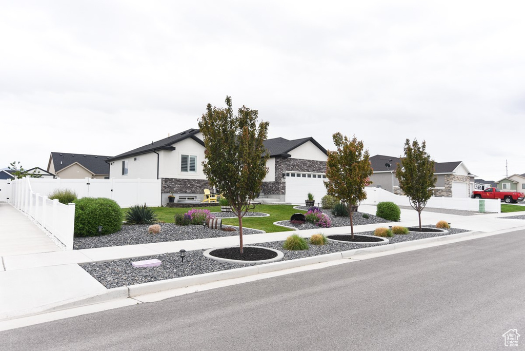 View of front of home with fence, stone siding, a residential view, and stucco siding