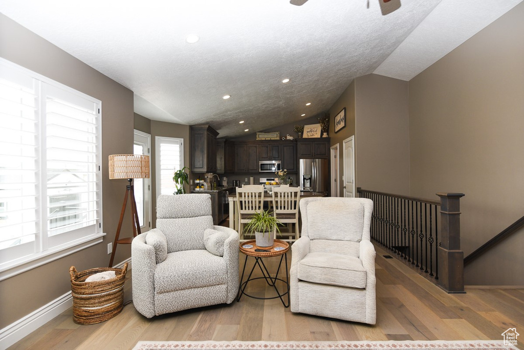 Sitting room featuring vaulted ceiling, light wood-type flooring, baseboards, an upstairs landing, and ceiling fan