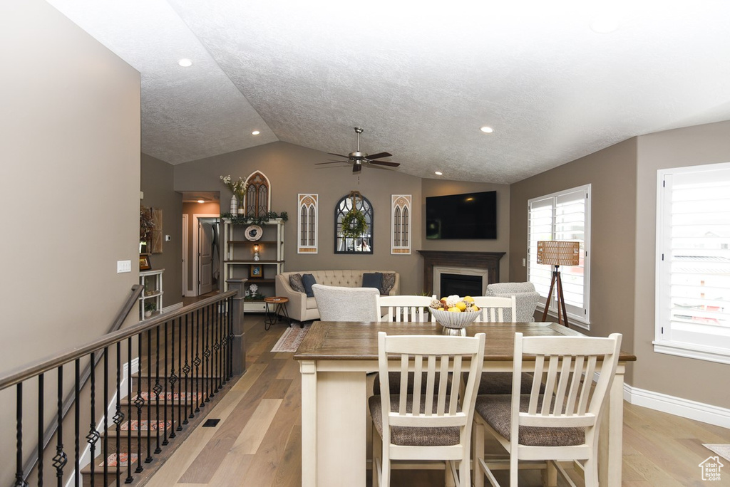 Dining room with light wood-style floors, lofted ceiling, a fireplace, a ceiling fan, and baseboards