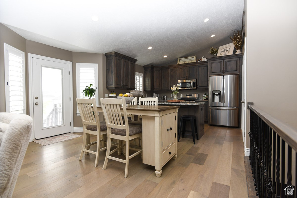 Kitchen with stainless steel appliances, a kitchen island, dark brown cabinetry, a kitchen bar, and light wood finished floors