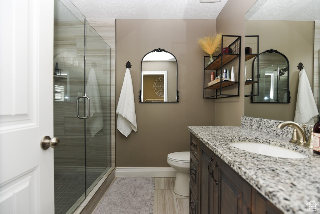 Bathroom with baseboards, a shower stall, toilet, vanity, and a textured ceiling
