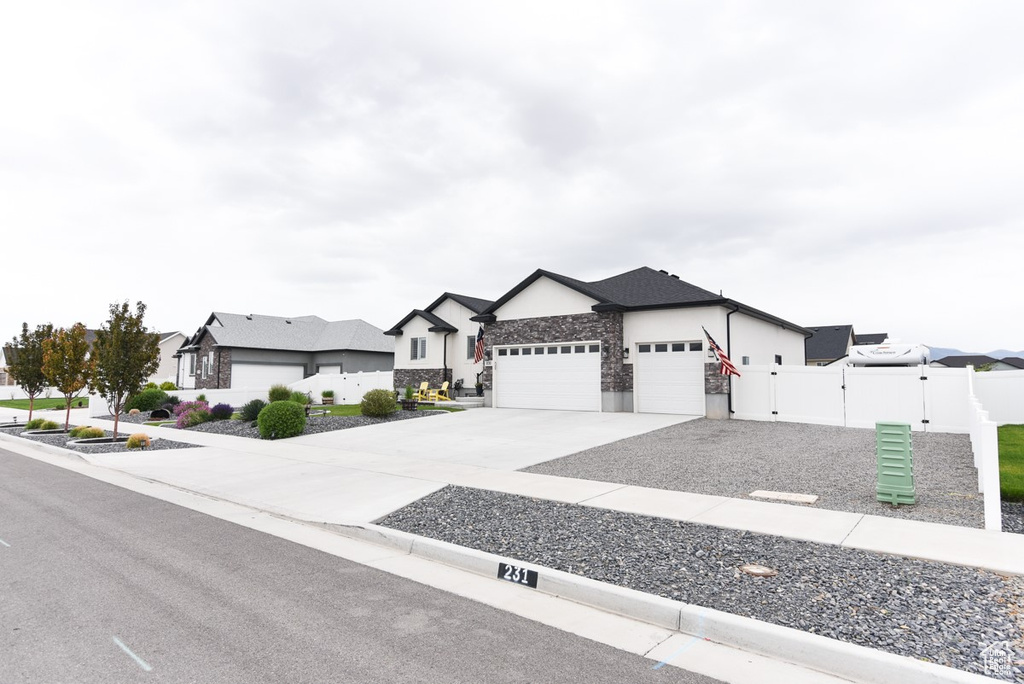 View of front of house with a garage, fence, driveway, stone siding, and stucco siding