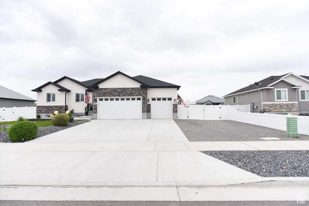 View of front of property featuring stone siding, a garage, fence, concrete driveway, and a gate