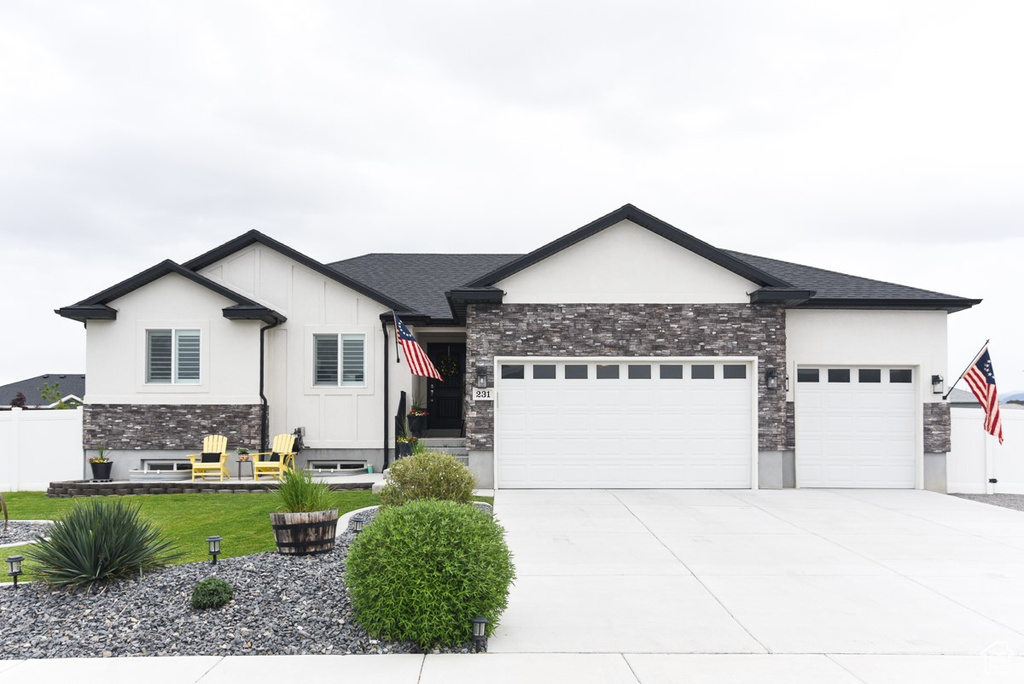 View of front facade with a garage, stone siding, concrete driveway, and a shingled roof