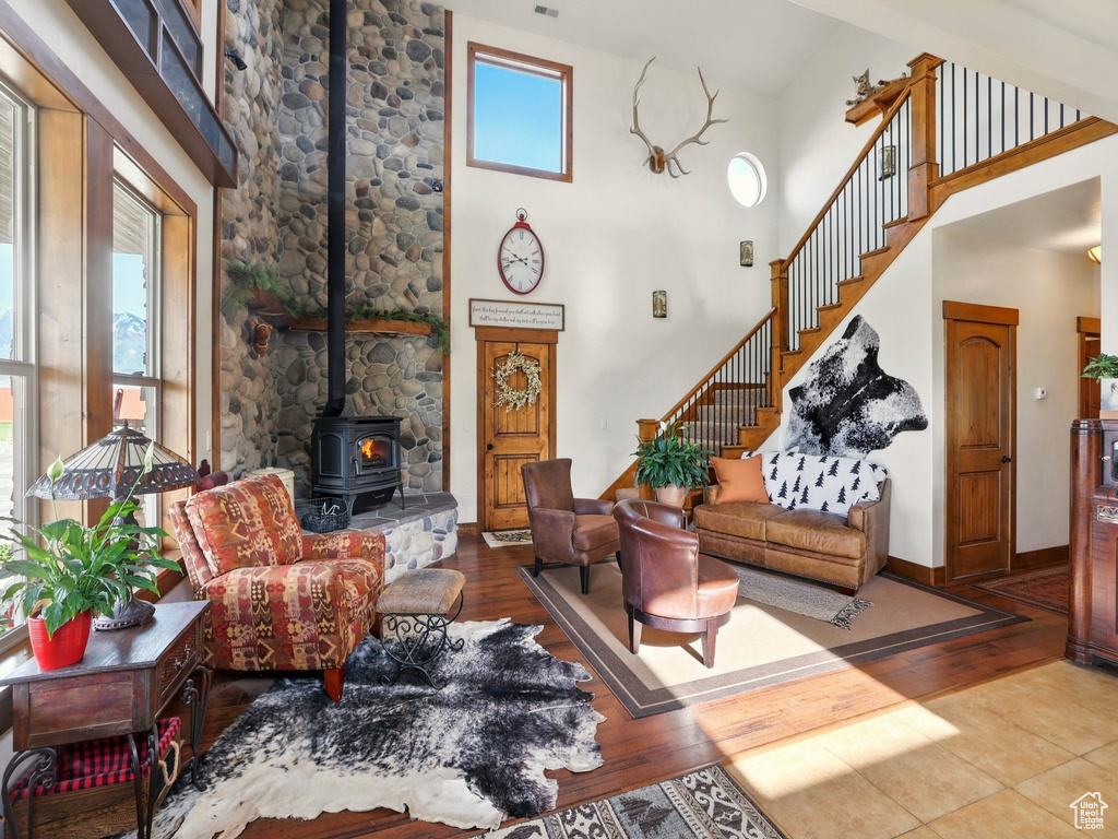 Living room featuring a wood stove, wood finished floors, stairs, a high ceiling, and baseboards