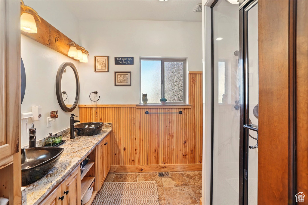 Full bathroom featuring a stall shower, a wainscoted wall, wood walls, and double vanity