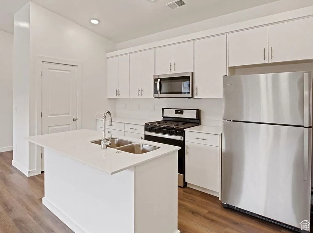 Kitchen featuring wood finished floors, a sink, a kitchen island with sink, stainless steel appliances, and white cabinets