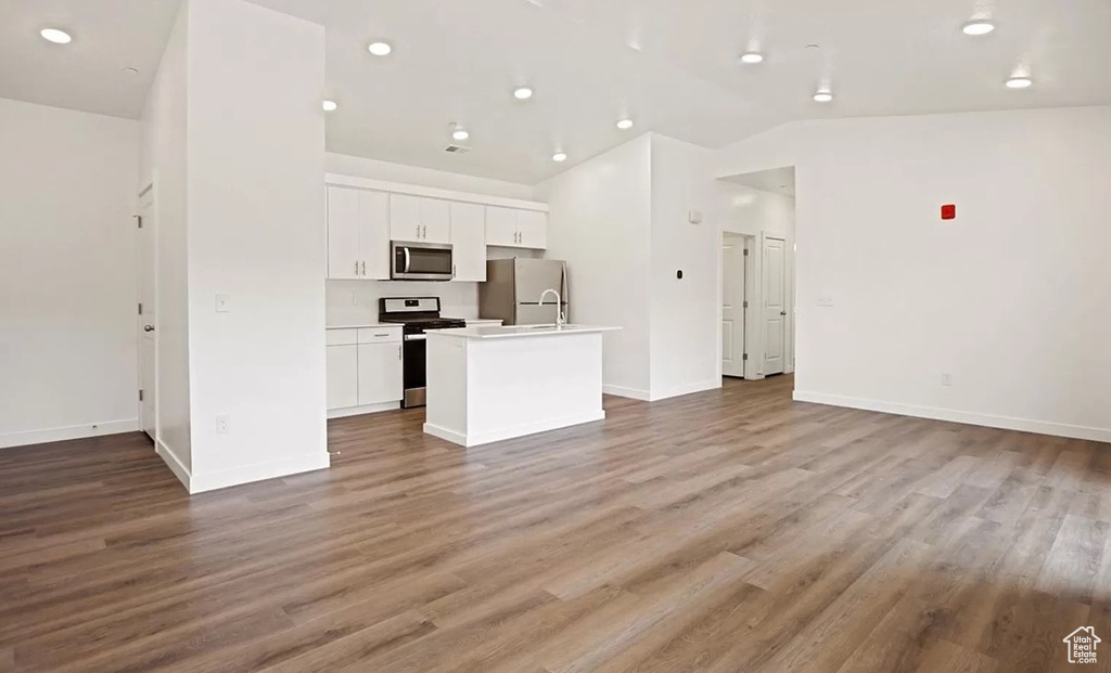 Kitchen featuring stainless steel appliances, a kitchen island with sink, open floor plan, and white cabinetry