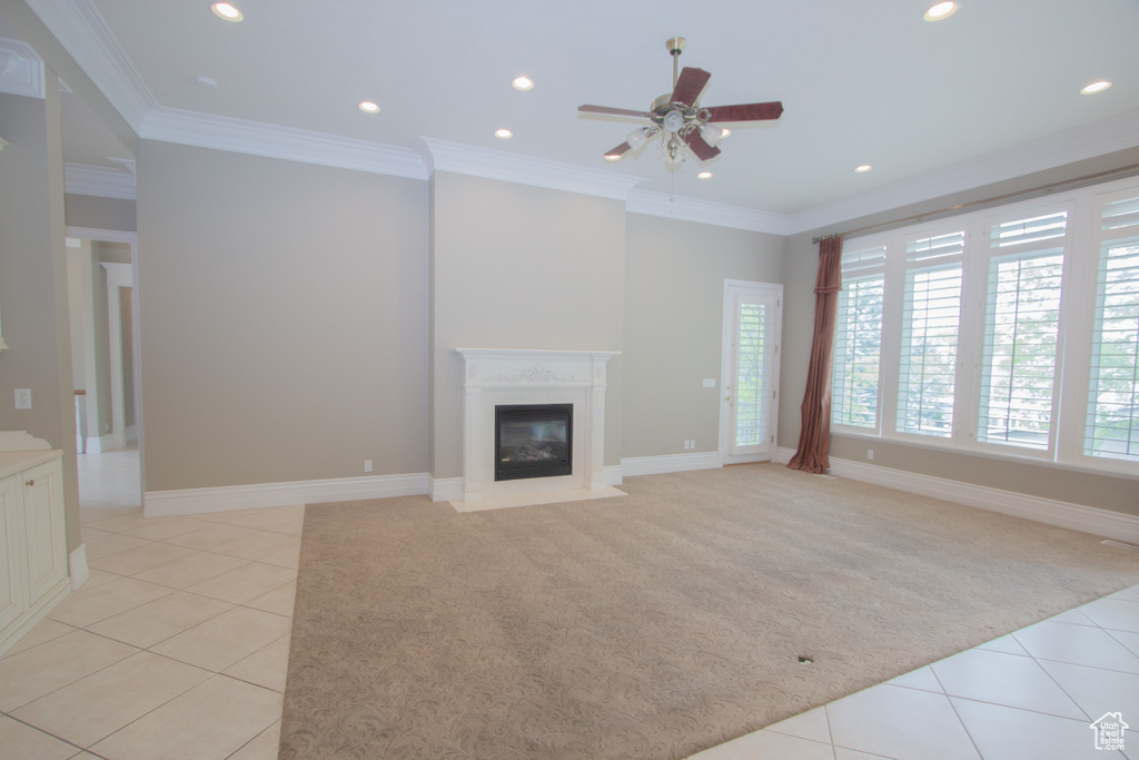 Unfurnished living room featuring light tile patterned flooring, light colored carpet, a ceiling fan, crown molding, and a fireplace with flush hearth