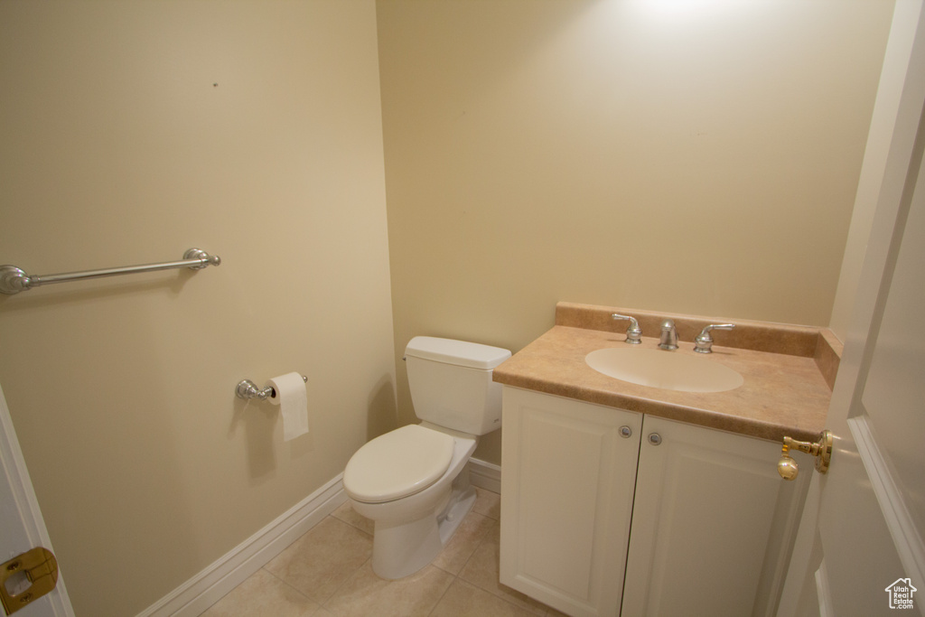 Half bath featuring toilet, vanity, tile patterned floors, and baseboards