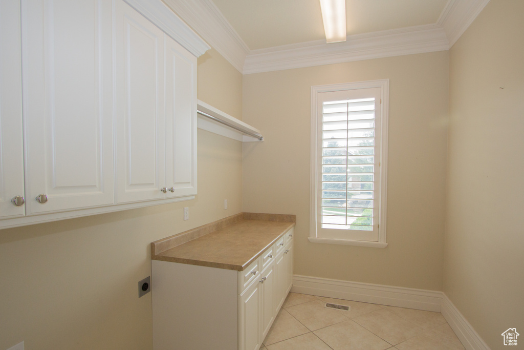 Laundry room featuring electric dryer hookup, crown molding, light tile patterned floors, baseboards, and cabinet space