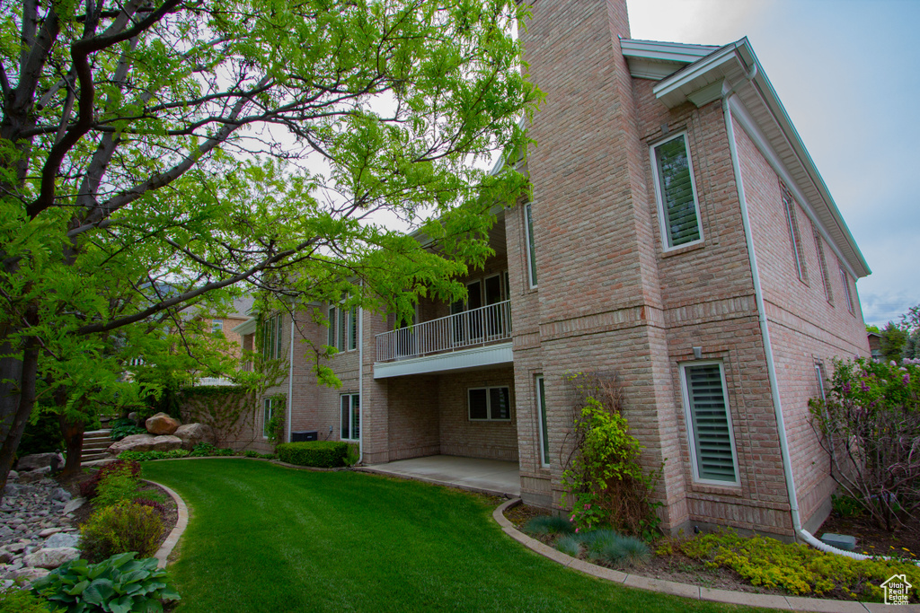 Rear view of house with a balcony, a patio, brick siding, a yard, and a chimney