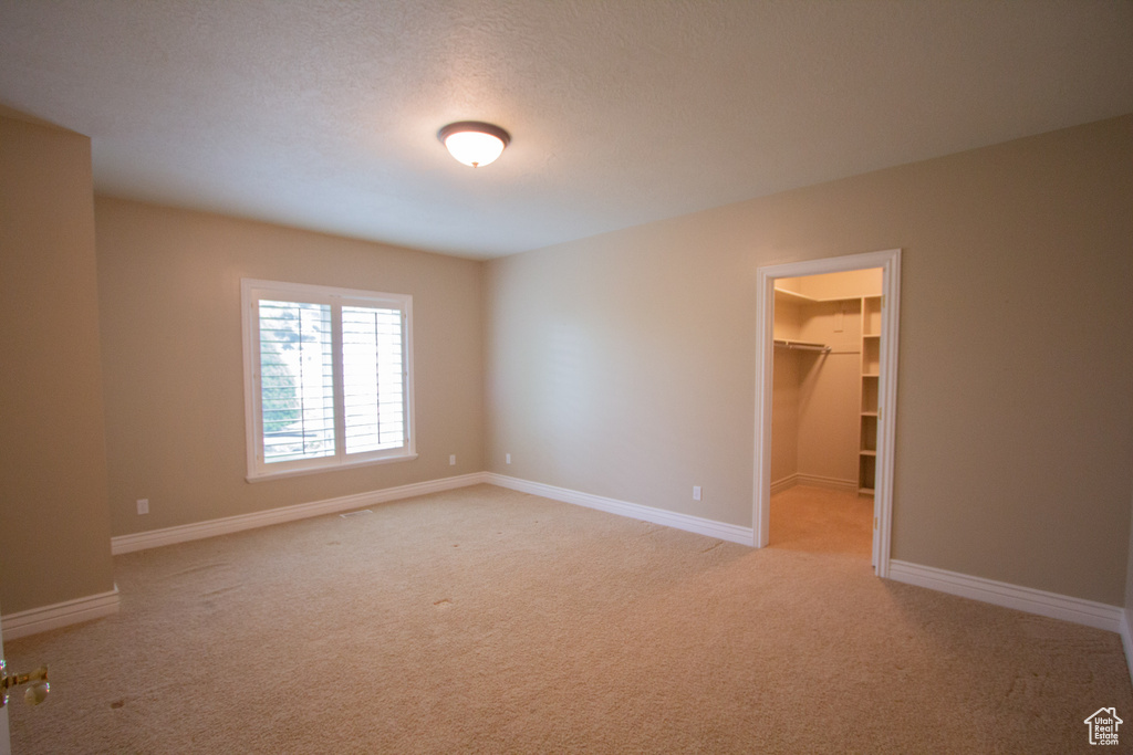 Unfurnished bedroom featuring light colored carpet, a spacious closet, baseboards, and a closet