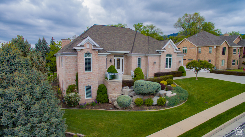 View of front facade featuring brick siding, a front yard, a chimney, and roof with shingles