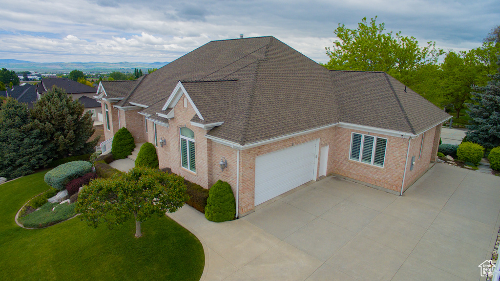 View of front of home featuring brick siding, an attached garage, a shingled roof, concrete driveway, and a front lawn