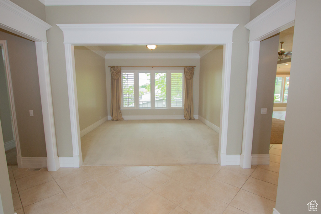 Hall with light carpet, crown molding, plenty of natural light, baseboards, and light tile patterned floors