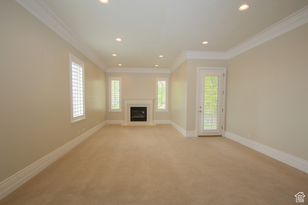 Unfurnished living room featuring recessed lighting, light colored carpet, a glass covered fireplace, baseboards, and crown molding