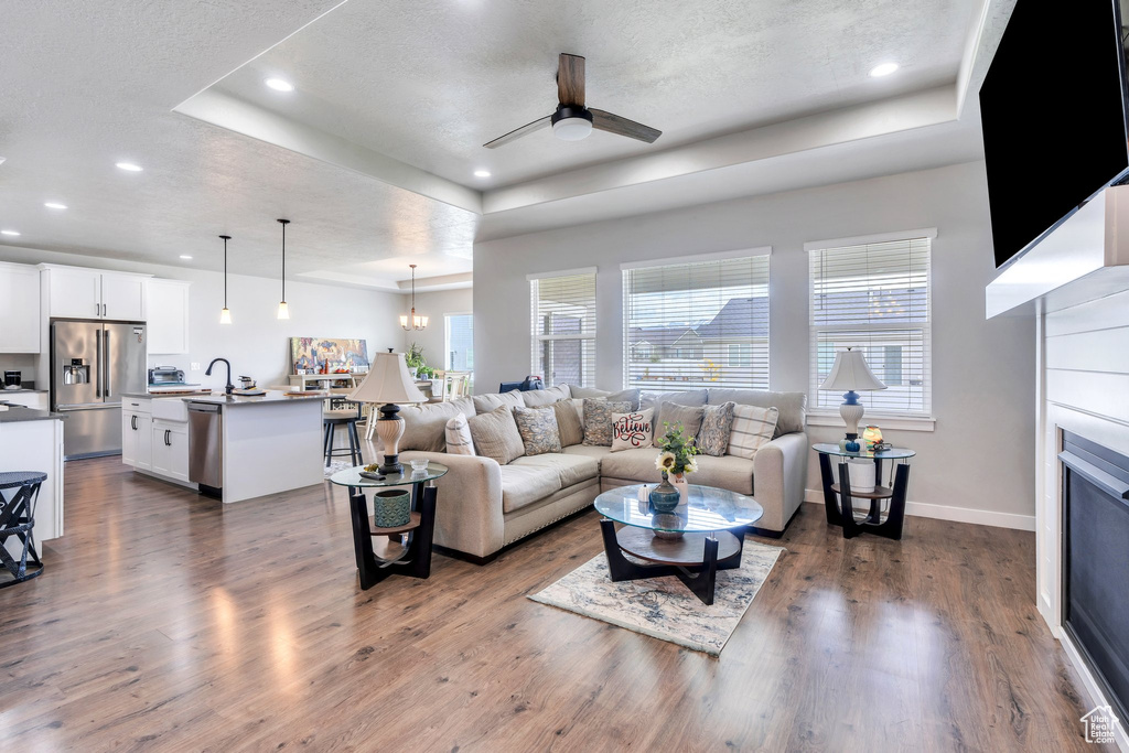 Living room featuring a raised ceiling, plenty of natural light, a ceiling fan, dark wood-style floors, and a textured ceiling