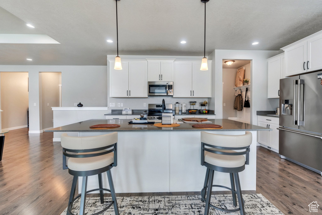 Kitchen with appliances with stainless steel finishes, dark countertops, wood finished floors, a kitchen bar, and recessed lighting