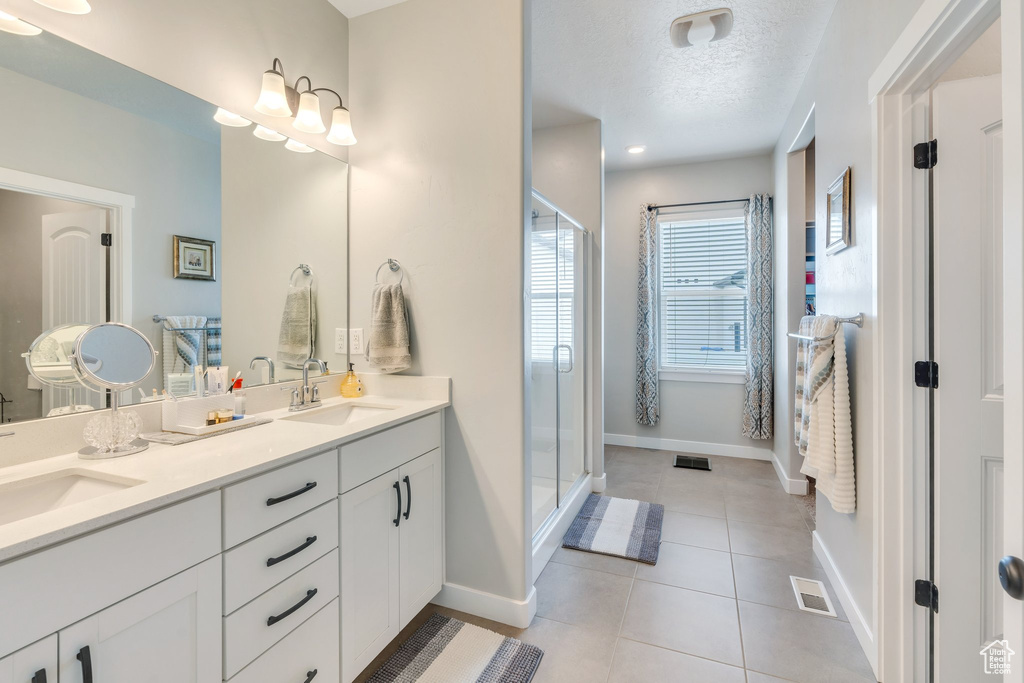 Bathroom with baseboards, a stall shower, tile patterned floors, double vanity, and a textured ceiling